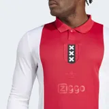 Camiseta de fútbol Adidas de manga larga, inspirada en el primer uniforme del Ajax de Ámsterdam, con diseño que combina un panel central rojo con mangas y costados blancos. Posee cuello de chomba rojo y puños acanalados rojos. En el pecho lleva el escudo conmemorativo del club con las tres cruces de Ámsterdam y el logo de Ziggo.