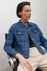 Chaqueta de jean azul medio, de corte clásico, con cuello camisero, bolsillos con solapa en el pecho y cierre frontal con botones metálicos color cobre.