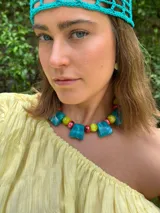 Collar corto con cuentas de resina cuadradas color turquesa, cuentas redondas de cerámica color verde lima con diseño floral rojo y tiento sintético con cierre ajustable.