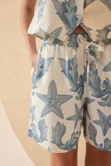 Short tipo bermuda de lino color crudo con estampado de estrellas de mar y hojas en color azul.