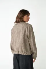 Campera estilo bomber de cuello redondo, color beige jaspeado, con cierre frontal de broches y bolsillos delanteros con ribete marrón.
