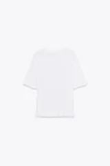 Top blanco de punto liso con cuello redondo y manga corta. Detalle de volantes en mangas y ruedo.