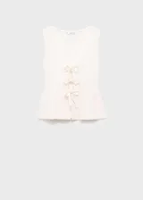 Top de punto fino color blanco hueso, sin mangas, con escote pronunciado en V y cierre frontal mediante lazos anudados. Presenta un tejido de canalé y un diseño ligeramente evasé en la parte inferior.