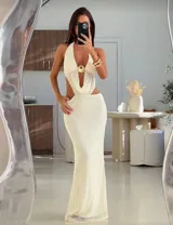 Vestido largo de tejido de punto color crema, con escote halter, espalda descubierta, abertura en la falda y detalle de aro dorado en el pecho.