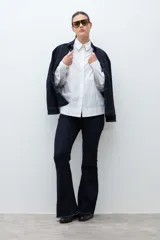 Camisa blanca de manga larga con puños fruncidos y cuello abotonado, corte holgado.