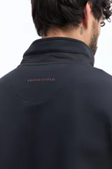 Campera de algodón gris azulado con cierre frontal completo y cuello alto. Presenta detalles de tela técnica azul verdoso en la parte superior del pecho y hombros, y un parche negro con texto blanco en el pecho izquierdo.