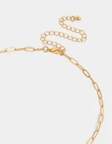 Collar corto dorado con cadena de eslabones y multidijes: candado con corazones dorados, dedal plateado, mano negra, cuentas de cristal, pez plateado, borla de cordones verdes y dije de luna plateada.