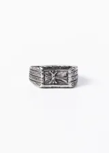 Anillo signet de acero quirúrgico pulido con cruz estilizada en relieve y grabados geométricos laterales.