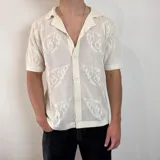Camisa tejida color crema con diseño calado, cuello tipo polo, manga corta y cierre frontal con botones.