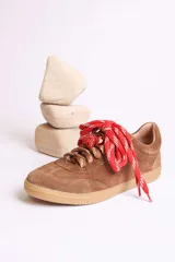 Zapatillas bajas marrones de gamuza con cordones y detalle de aplique de fresa en los cordones.