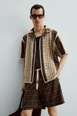 Camisa de hombre de corte relajado, confeccionada en tejido de crochet con estructura abierta. Presenta cuello bowling, manga corta y cierre frontal con botones.