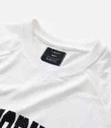 Remera de hombre con corte boxy, confeccionada en tejido mesh (malla) blanco, con cuello en V y estampa arqueada en negro que dice "NEW YORK CITY ATHLETICS".