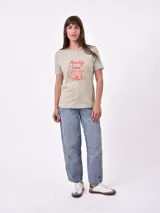 Remera blanca de algodón con cuello redondo y manga corta. Presenta un pequeño bordado en el pecho izquierdo con una figura que parece ser una persona acostada en una tabla de surf o flotador.