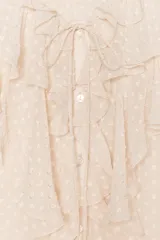 Blusa color crema semitransparente con cuello redondo con volantes y cordón. Manga larga acabada en elástico y volante. Cierre frontal con botones.