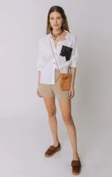 Camisa color naranja de lino o algodón con cuello clásico, cierre frontal con botones y mangas largas con puños abotonados. Presenta un bolsillo de cuero marrón en el pecho.