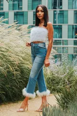 Pantalón de denim celeste con corte acampanado y detalle de plumas blancas en el ruedo.