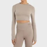 Top deportivo color beige, de manga larga, corte cropped y calce ajustado.