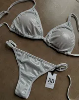 Conjunto de bikini plateado brillante, compuesto por un corpiño triangular con tirantes finos y una bombacha tipo colaless con tiras laterales ajustables.