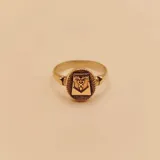 Anillo dorado con diseño de escudo con símbolos de contaduría.