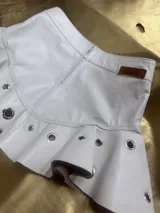 Mini pollera blanca de cuero con volados y apliques metálicos circulares.