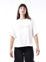 Remera blanca de corte holgado con mangas cortas y estampado frontal con la palabra "Botanical" en letras cursivas plateadas.