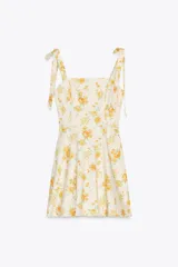 Vestido corto de popelina color crema con estampado de rosas amarillas, escote recto y tirantes con lazos. Tiene forro interior y cierre trasero con cremallera oculta.
