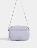 Bandolera gris claro de tela deportiva con bolsillo frontal, correa larga regulable, acceso con cierre superior y tag de goma.