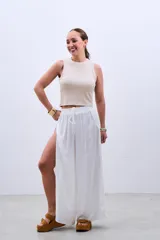 Pantalón blanco de tela fluida con cintura elastizada y cordón ajustable. Presenta aberturas laterales amplias desde la cintura hasta el ruedo.