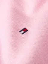 Chomba rosada de Tommy Hilfiger, modelo 1985, de corte regular, con cuello tipo chomba, cartera de dos botones, mangas cortas y logo bordado en el pecho. El interior del cuello es rayado.