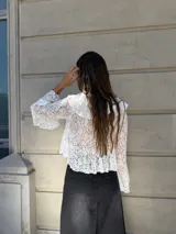 Blusa de encaje blanco con volados en el escote y mangas acampanadas. Se ata en el frente con lazos.
