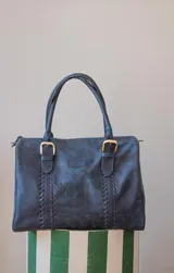 Bolso de mano azul con detalles de costuras verticales y herrajes dorados.