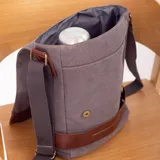 Morral gris de tela canvas con detalles en cuero marrón. Tiene correa larga regulable, tapa con broches magnéticos, bolsillo tipo guantera bajo la tapa, división interna con velcro y bolsillo trasero con broche magnético.