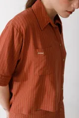 Camisa corta de manga corta color rojo, con doble cartera diagonal con botones de madera, cuello clásico y botamangas marcados. Tiene un bolsillo con aplique de crochet hecho a mano con forma de frutilla.