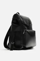 Mochila negra de cuero sintético con solapa y cierre magnético. Tiene un compartimento principal con espacio para dispositivos electrónicos de hasta 13 pulgadas y un bolsillo con cierre. En la parte frontal tiene un bolsillo con cierre y bolsillos planos en los laterales. La parte posterior es acolchada y tiene una banda de sujeción para equipaje. Tiene asa de mano y dos asas de hombro ajustables y acolchadas.