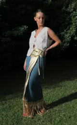 Minifalda azul con textura brillante y flecos dorados en el ruedo. Presenta un cinturón ancho dorado que se anuda al frente.
