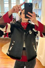 Chaleco bomber de cuero negro con cuello y borde inferior de piel sintética negra. Tiene cierre frontal con cremallera y detalles de estampado animal print en los laterales.