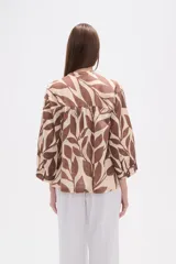 Camisa holgada con estampado de hojas en tonos marrones y beige, cuello mao, cierre frontal con botones y un bolsillo en el pecho.
