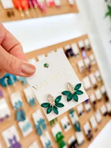 Par de caravanas doradas con forma de flor, con incrustaciones de cristales verdes y blancos.