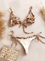 Conjunto de bikini color marrón con estampado de pequeñas flores blancas. El corpiño es de triángulo con tiras finas que se atan al cuello y a la espalda. La bombacha es colaless con tiras finas que se atan a los costados.