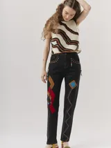 Pantalón de jean azul con parches de colores, tiro alto, corte mom-fit, apliques de cuero trenzado alrededor de los bolsillos frontales y canutillos en la parte frontal.