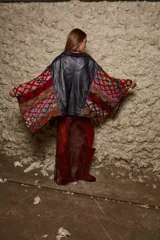 Chaqueta negra de cuero con corte clásico, cuello camisero, cierre frontal con botones y bolsillos con solapa en el pecho. Las mangas son tejidas en lana con diseño geométrico en tonos rojo, marrón, blanco y azul.