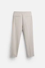 Pantalón color arena de corte recto, confeccionado en tejido elástico. Cuenta con cintura elástica ajustable con cordón, bolsillos laterales y bolsillos de vivo en la parte trasera.