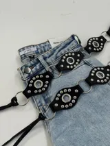 Cinto negro de cuero sintético con apliques de tachas plateadas y argollas metálicas.