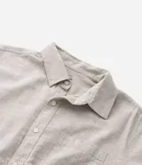 Camisa de hombre de manga corta color arena, confeccionada en lino y algodón. Tiene cuello camisero, corte clásico, cierre frontal con botones, un bolsillo en el pecho y ruedo recto.