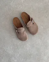 Zuecos marrones de gamuza con hebilla metálica ajustable.