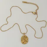 Collar dorado con dije ovalado texturizado con incrustaciones de circonitas en forma de luna creciente, ojo turco y estrellas de diferentes tamaños.