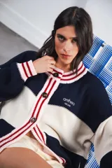 Cardigan de punto grueso, estilo universitario, con bloques de color azul marino y crema. Presenta cuello, puños y tapeta de botones en punto acanalado con franjas rojas y rosadas. Cierre frontal con botones marrones.