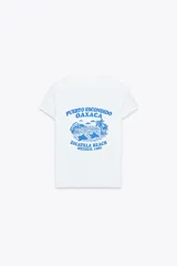 Remera blanca de corte slim fit, cuello redondo y manga corta. Estampado frontal con texto en azul que dice 'Puerto Escondido Oaxaca Zicatela Beach Mexico, 1980'.