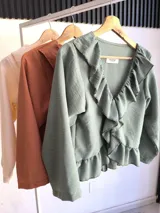 Blusa verde agua con cuello camisero con volados, mangas largas con puños elásticos y corte a la cintura.