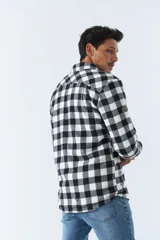 Sobrecamisa de algodón para hombre con interior de corderito, estampado a cuadros en tonos negro, blanco y azul. Tiene cierre de botones, bolsillos tipo cartera y logo en goma. El modelo usa talle M.